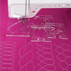 the sewing machine is next to some cut out shapes on the pink tablecloth that's being sewn