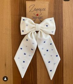 a white bow with blue hearts on it sitting on top of a wooden floor next to a sign