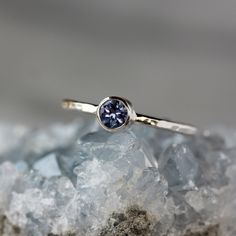 A gorgeously hued, violet-blue Tanzanite gemstone is set entirely in sterling silver. The bezel is integrated right into the band, which I hand-hammer for a sparkling, faceted finish. Tanzanite has a color all its own--unmatched by other gemstones--and pairs beautifully with sterling silver. It is a very rare stone, and the mine supply will soon run out. This genuine Tanzanite gemstone measures 4mm in diameter, and the sterling silver band measures just under 2mm thick. This ring is made to orde Silver Tanzanite Solitaire Jewelry, Sterling Silver Sapphire Ring With Bezel Setting, Tanzanite Bezel Setting Promise Ring, Bezel Set Tanzanite Jewelry For Anniversary, Blue Amethyst Ring With Accent Stones In Sterling Silver, Anniversary Tanzanite Jewelry With Bezel Setting, Ethical Tanzanite Birthstone Ring, Blue Amethyst Ring In Sterling Silver For Gift, Tanzanite Amethyst Birthstone Ring As Gift