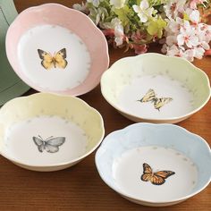 four bowls with butterflies painted on them sitting on a table next to flowers and a vase