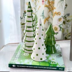 three ceramic christmas trees sitting on top of a table next to a book and vase