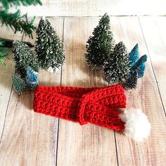 a red knitted hat with white pom - pom on it next to christmas trees