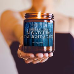 a woman holding a candle that says smells like i'm watching twilight again on it