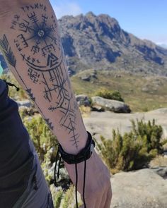 a man with a tattoo on his arm holding onto a mountain range in the background