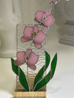 a glass vase with pink flowers in it sitting on a wooden stand next to a white wall