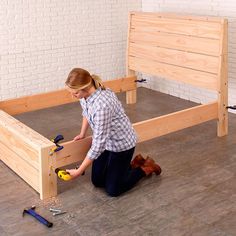 a woman kneeling down on the ground working on a bed frame with tools and hammers