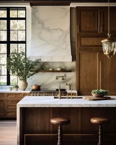 a kitchen with marble counter tops and wooden cabinets, two stools in front of the sink