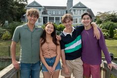 three boys and a girl standing on a bridge in front of a house