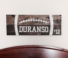 a bed with a wooden headboard and football sign on the wall above it that says duranso