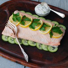 a piece of salmon with cucumber and lemon slices on a wooden platter