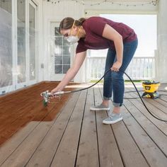 a woman using a pressure washer on a wooden floor in front of a window