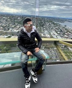 a man sitting on top of a tall building next to a glass floored walkway