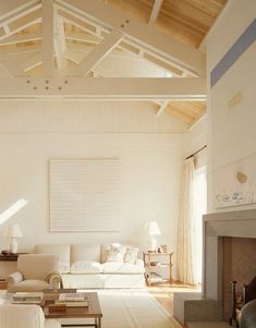 a living room with white furniture and wood beams on the ceiling is lit by sunlight coming through the windows