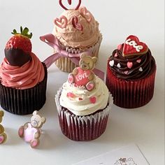 four cupcakes with chocolate frosting and pink icing, one decorated like a teddy bear