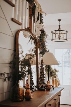 a mirror sitting on top of a wooden dresser next to a lamp and christmas decorations