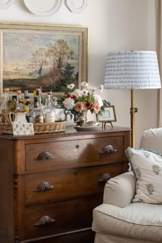 an old dresser with flowers and bottles on it in front of a wall hanging above