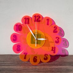 a colorful clock with numbers on it sitting on top of a wooden table in front of a white wall