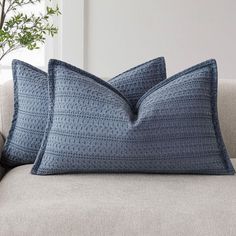 two blue pillows sitting on top of a couch next to a plant in a vase