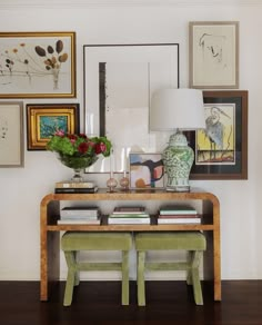 a table with two stools in front of pictures on the wall and paintings above it