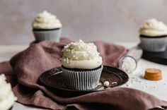 three cupcakes with white frosting on a black plate next to a brown napkin