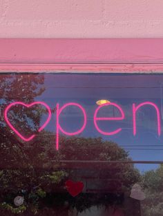 a pink neon sign that says open in front of a window