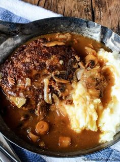 a bowl filled with mashed potatoes, meat and gravy on top of a wooden table