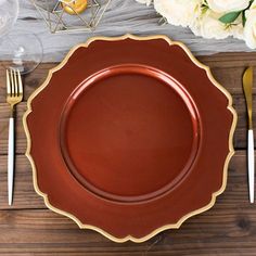 a brown plate with gold trim sits on a wooden table next to silverware and flowers