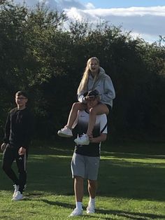 a man is carrying a woman on his shoulders in the middle of a grassy field