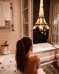 a woman sitting in a bathtub looking at the eiffel tower