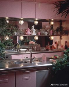 a kitchen with pink cabinets and lights above the sink, potted plants on the counter