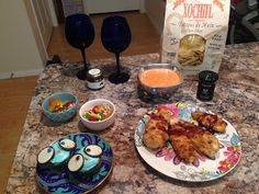 a table topped with plates and bowls filled with food next to wine glasses on top of a counter