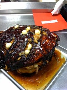 a large piece of meat sitting on top of a metal pan covered in sauce and nuts