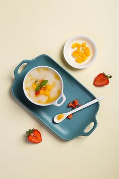 there is a bowl of soup and two bowls of fruit on the tray with spoons