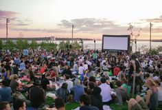 a large group of people sitting on top of a grass covered field next to water