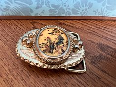 a brooch sitting on top of a wooden table next to a flowered wall