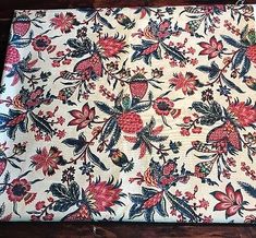 an old table cloth with flowers and leaves on it, sitting on top of a wooden floor