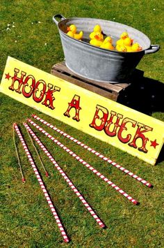 a sign that says hook a duck next to four rubber ducks in a bucket on the grass