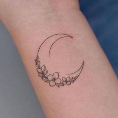 a small tattoo on the wrist of a woman's left arm with flowers and a crescent