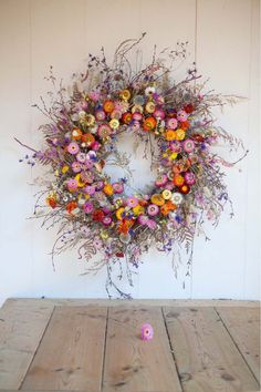 a floral wreath on a wooden table against a white wall with pink and orange flowers