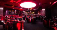 the interior of a nightclub with red lighting and black seats, bars and stools