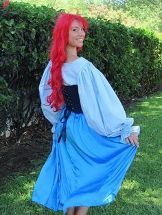 a woman with red hair and blue dress posing for the camera in front of bushes