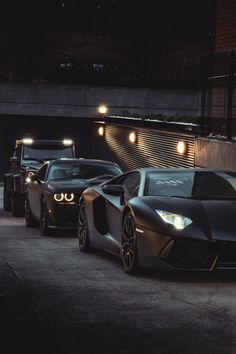 two black sports cars parked next to each other in front of a building at night