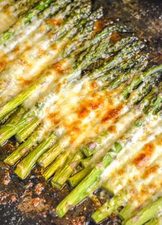 asparagus being cooked in a skillet with melted cheese and sauce on top