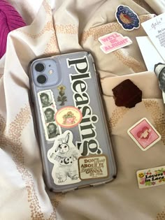 an iphone case sitting on top of a bed covered in stickers and magnets