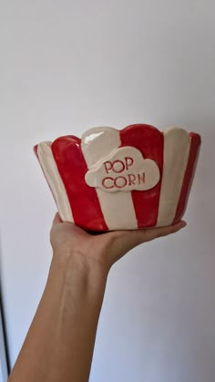 a hand holding a red and white striped cup with the word pop corn on it