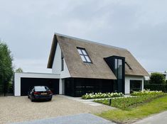 a car is parked in front of a house with a thatched roof and black shutters