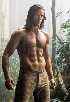 a man with long hair and no shirt standing in the jungle