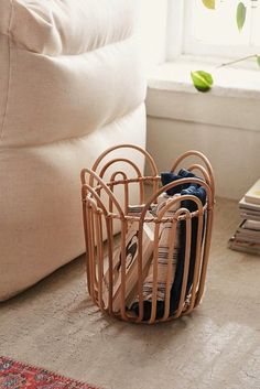 a wooden basket filled with clothes on top of a floor next to a white couch