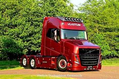 a red semi truck parked on the side of a road next to some green trees