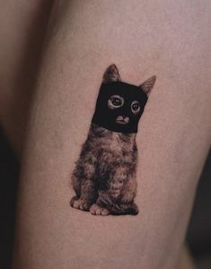 a small black and grey kitten tattoo on the thigh, with an eyeball in it's eyes